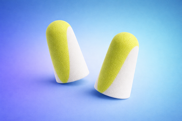 Pair of super soft foam earplugs in yellow and white, designed for gentle noise reduction and comfortable sleep, displayed on a blue gradient background.